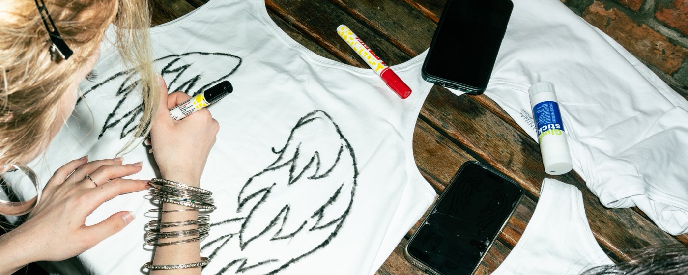 Hands drawing a design onto a white vest with a marker pen at the painting table.