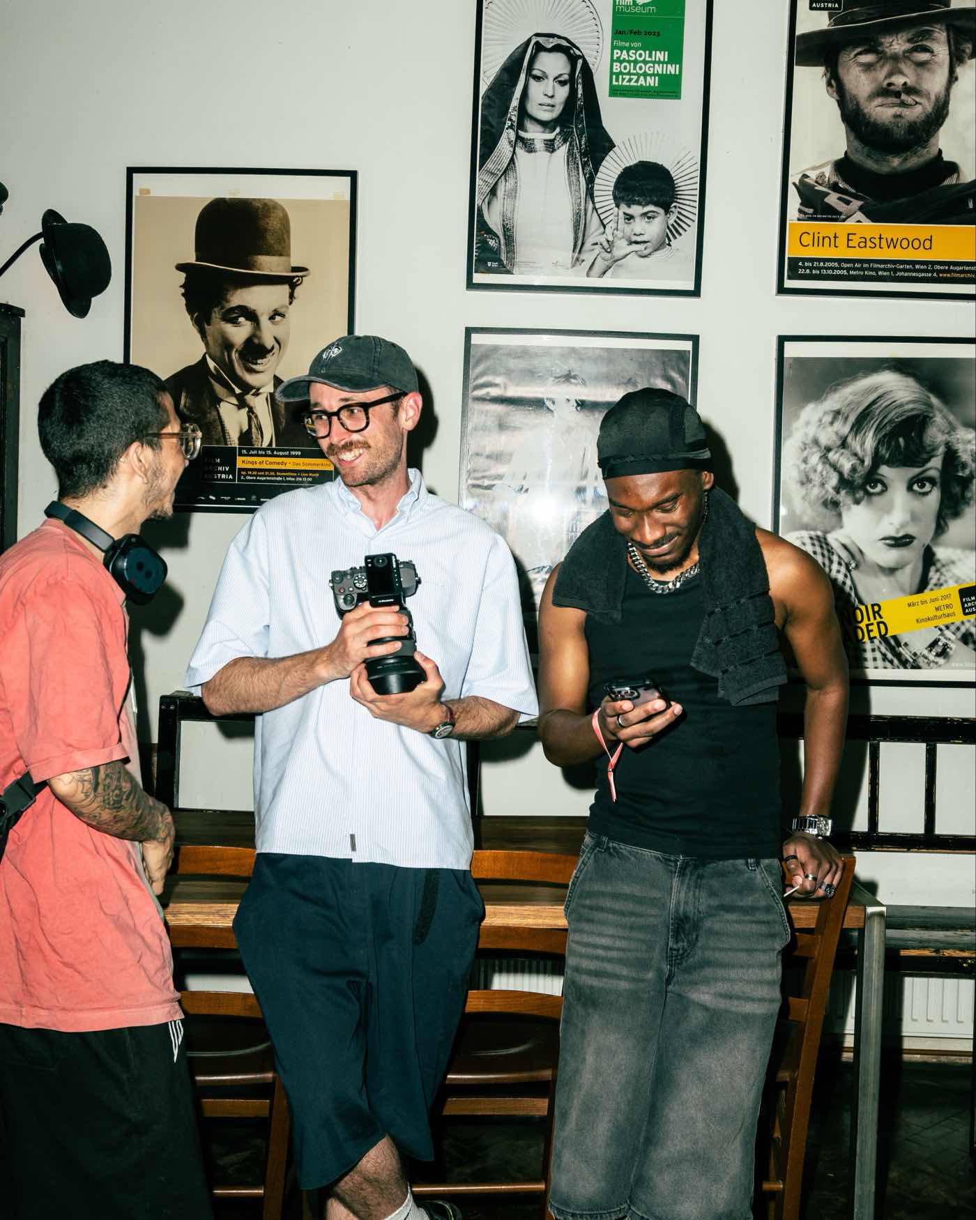 Three guests talking beside a wall of framed film posters, one holding a camera.