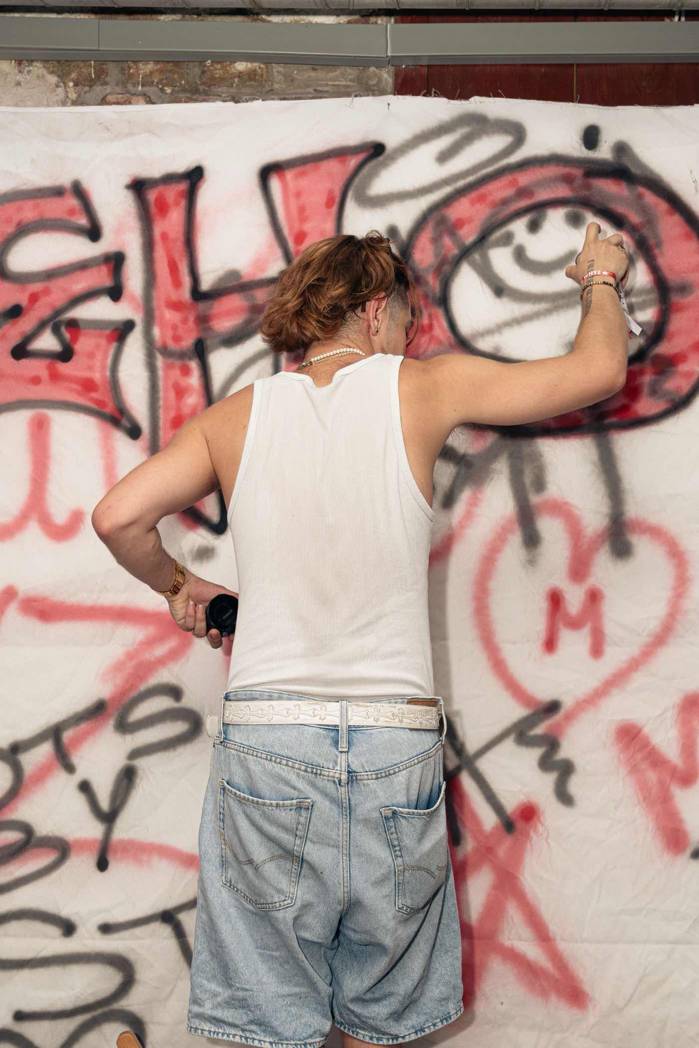 A guest spray-painting a large red letter onto the paint wall, seen from behind.